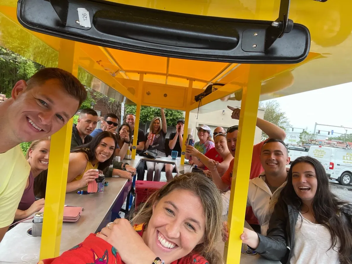 A full group smiling together aboard the yellow Pensacola Pedal Trolley